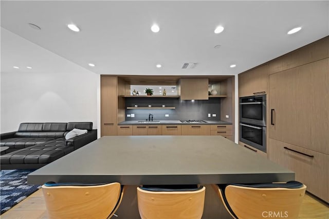 kitchen with double oven, sink, stovetop, a center island, and light hardwood / wood-style floors