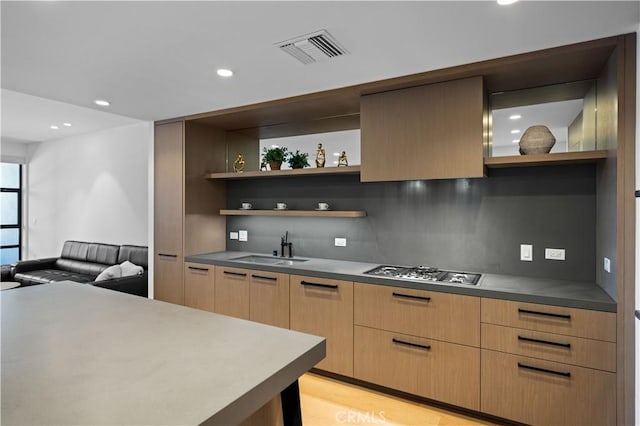 kitchen with stainless steel gas stovetop, light brown cabinets, backsplash, sink, and light wood-type flooring