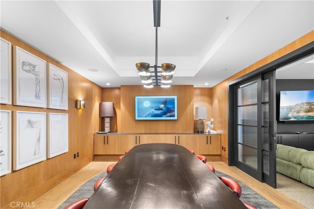 interior space with a tray ceiling, an inviting chandelier, wood walls, and light hardwood / wood-style flooring