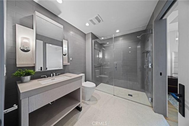 bathroom with vanity, toilet, a shower with door, and tile walls