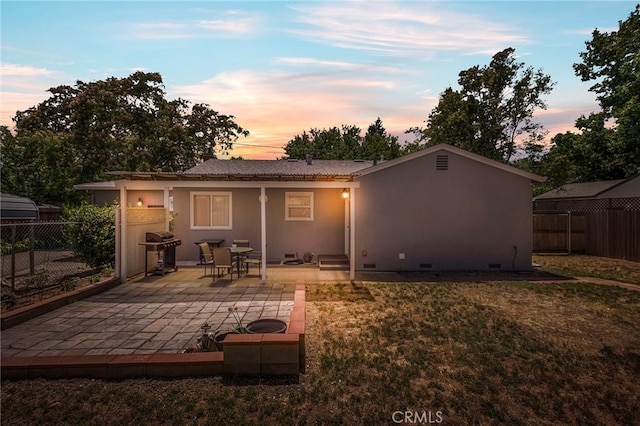 back house at dusk with a lawn and a patio area