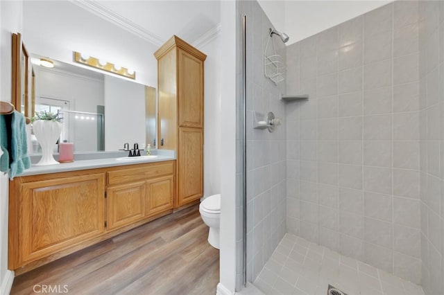 bathroom featuring toilet, hardwood / wood-style flooring, a tile shower, ornamental molding, and vanity