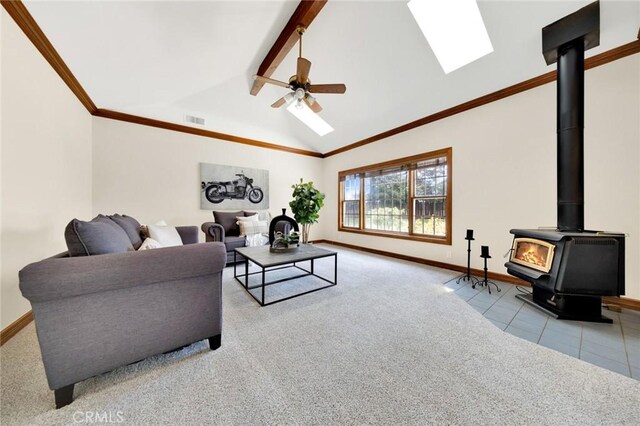 living room featuring light carpet, ceiling fan, a wood stove, and vaulted ceiling with beams