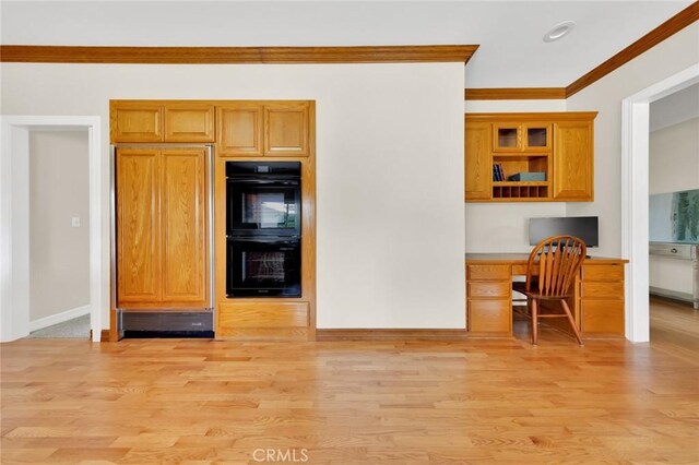 kitchen featuring light wood-type flooring, paneled fridge, crown molding, double oven, and built in desk