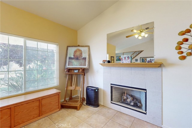 living area with ceiling fan, light tile patterned floors, a tile fireplace, and vaulted ceiling