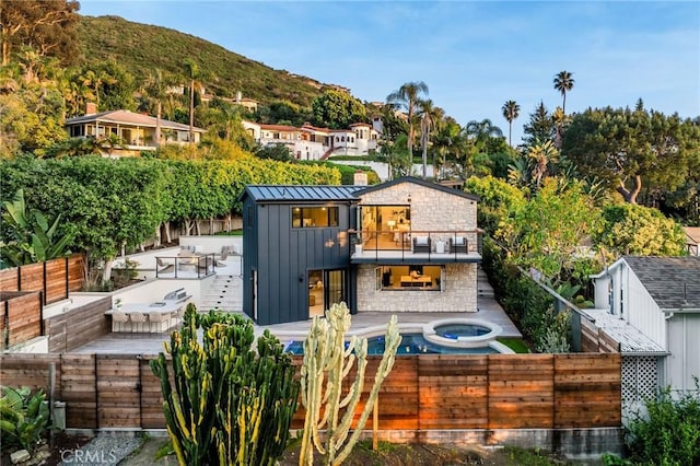 rear view of property with a mountain view, a balcony, an in ground hot tub, and a patio area