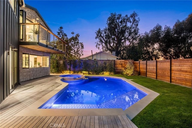 pool at dusk featuring a lawn and an in ground hot tub