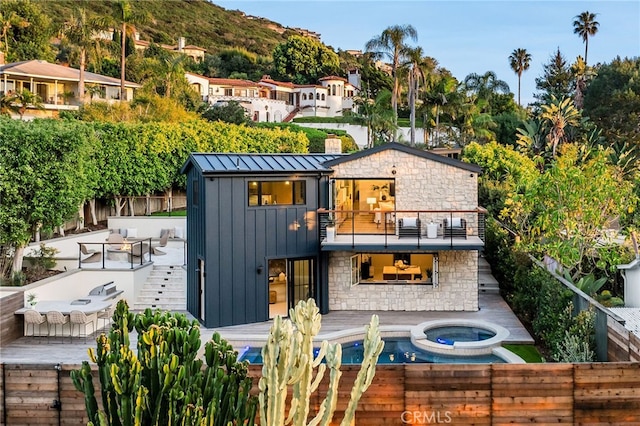 back of house featuring a balcony, an in ground hot tub, and a patio