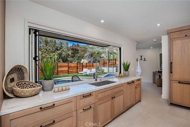 kitchen with light brown cabinetry, light stone countertops, and sink