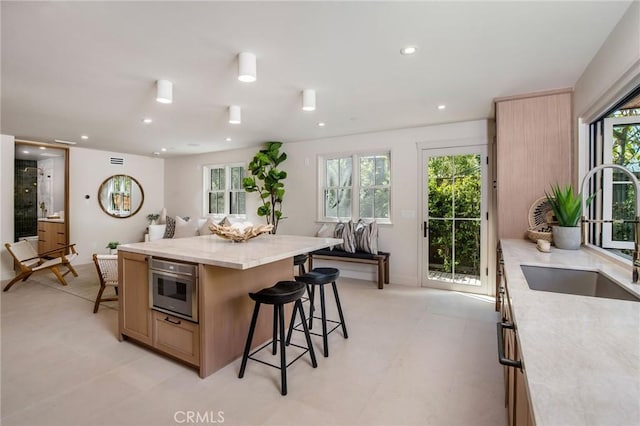 kitchen featuring light brown cabinets, sink, light stone countertops, a kitchen island, and a kitchen bar