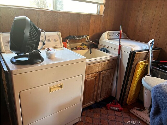 laundry area featuring dark tile patterned flooring, sink, wooden walls, and washing machine and clothes dryer