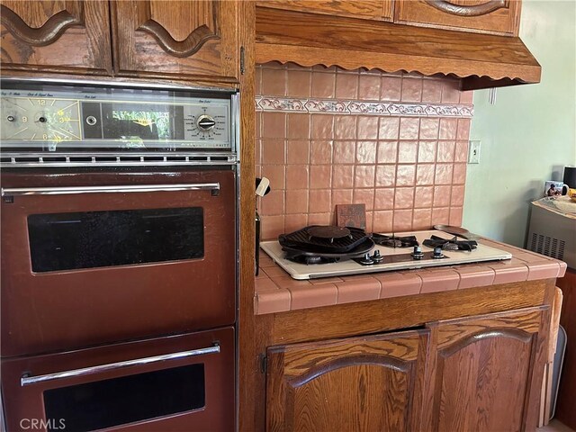 kitchen featuring tile countertops, white gas stovetop, black double oven, and tasteful backsplash