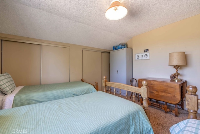 carpeted bedroom featuring vaulted ceiling, two closets, and a textured ceiling