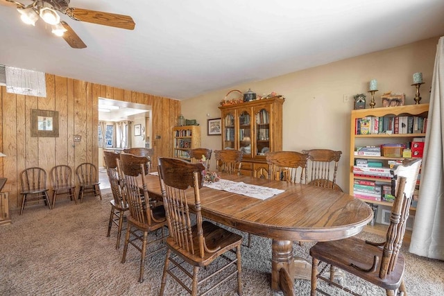 dining room with carpet floors, ceiling fan, and wooden walls