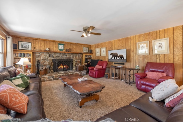 carpeted living room with a stone fireplace, ceiling fan, and wood walls