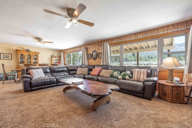 carpeted living room featuring ceiling fan and wood walls