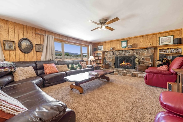 carpeted living room featuring ceiling fan, a stone fireplace, and wooden walls