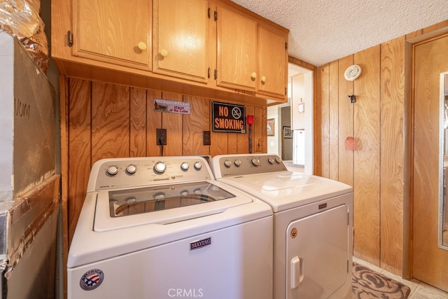 washroom featuring cabinets, wood walls, a textured ceiling, washer and clothes dryer, and light tile patterned floors