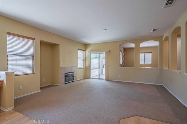 unfurnished living room with a tiled fireplace and light carpet