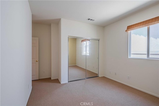 unfurnished bedroom featuring multiple windows, light colored carpet, and a closet