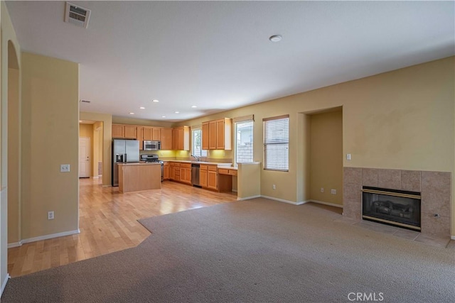 kitchen with sink, a tile fireplace, a kitchen island, light colored carpet, and stainless steel appliances