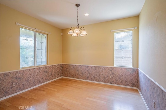 spare room featuring wood-type flooring, a wealth of natural light, and a notable chandelier