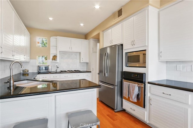 kitchen with sink, stainless steel appliances, backsplash, light hardwood / wood-style floors, and white cabinets