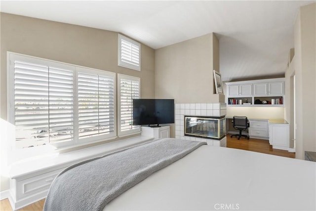 bedroom with a tile fireplace, hardwood / wood-style flooring, and multiple windows