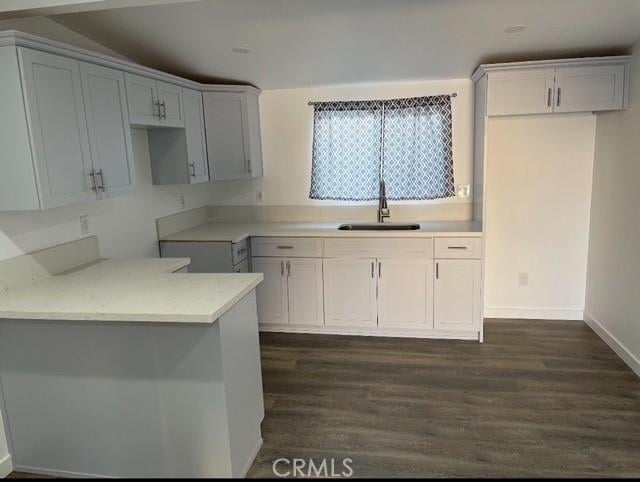 kitchen featuring white cabinetry, sink, dark wood-type flooring, kitchen peninsula, and vaulted ceiling