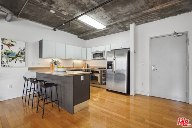 kitchen with white cabinetry, light hardwood / wood-style flooring, kitchen peninsula, a kitchen bar, and appliances with stainless steel finishes