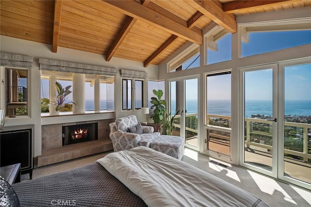 carpeted bedroom with a water view, wood ceiling, access to outside, a tile fireplace, and beamed ceiling