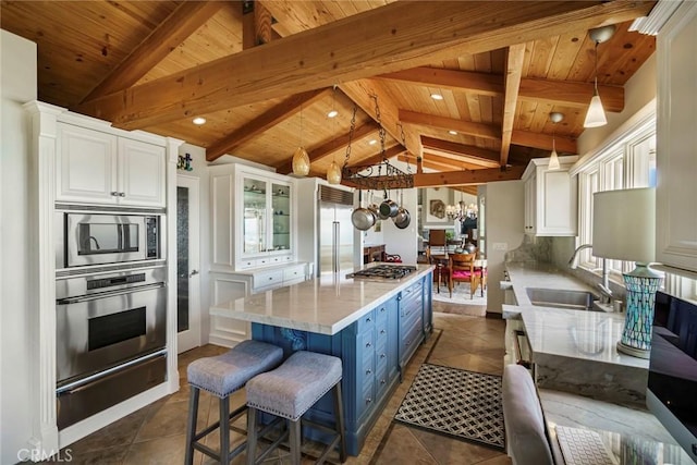 kitchen with sink, white cabinetry, built in appliances, decorative light fixtures, and lofted ceiling with beams