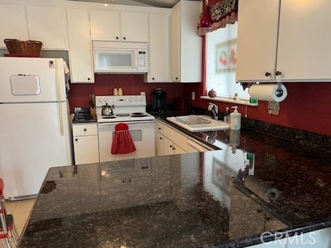 kitchen featuring sink, kitchen peninsula, white appliances, dark stone counters, and white cabinets