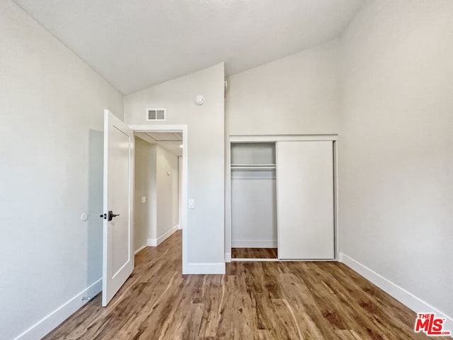 unfurnished bedroom featuring wood-type flooring, vaulted ceiling, and a closet