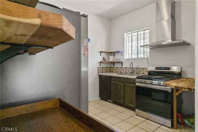 kitchen featuring light tile patterned flooring, sink, dark brown cabinets, gas range, and wall chimney range hood