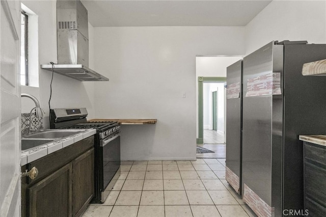 kitchen featuring light tile patterned flooring, dark brown cabinets, wall chimney exhaust hood, appliances with stainless steel finishes, and tile countertops