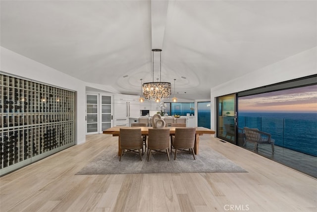 dining area featuring a water view, an inviting chandelier, and light hardwood / wood-style flooring