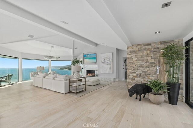 living room featuring light wood-type flooring, vaulted ceiling with beams, a water view, and a chandelier