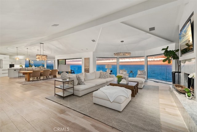 living room featuring light hardwood / wood-style flooring, vaulted ceiling, a premium fireplace, and a notable chandelier