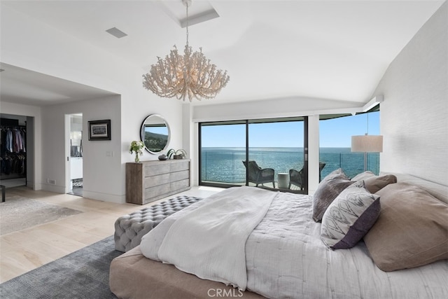 bedroom with light hardwood / wood-style floors, a water view, vaulted ceiling, a spacious closet, and a notable chandelier