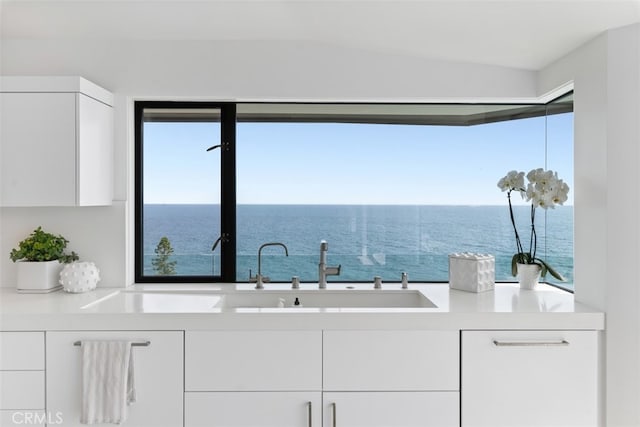 interior space featuring vaulted ceiling, white cabinets, sink, and a water view