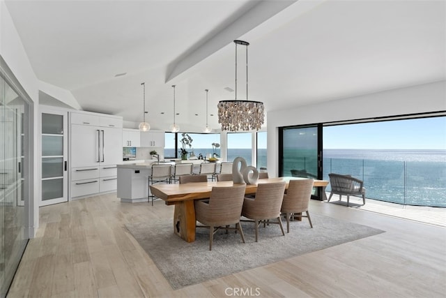 dining area with an inviting chandelier, a water view, light hardwood / wood-style floors, and vaulted ceiling