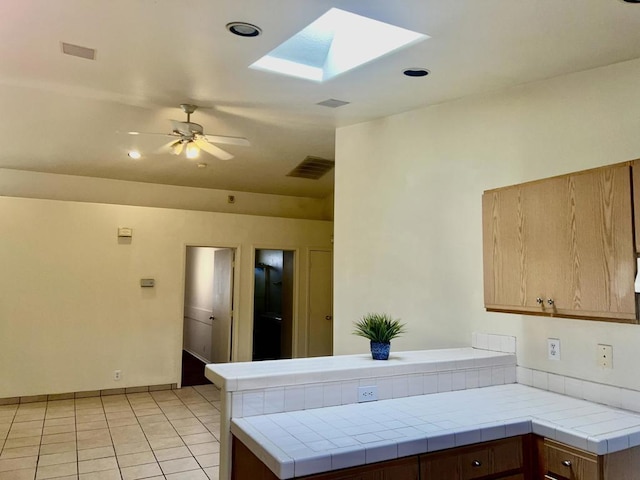 kitchen featuring a skylight, ceiling fan, kitchen peninsula, tile countertops, and light tile patterned flooring