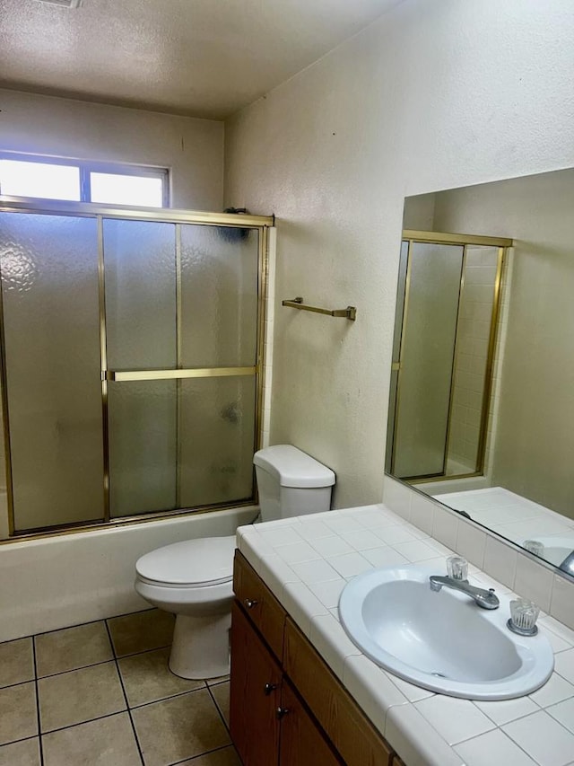 full bathroom with a textured ceiling, vanity, shower / bath combination with glass door, tile patterned flooring, and toilet