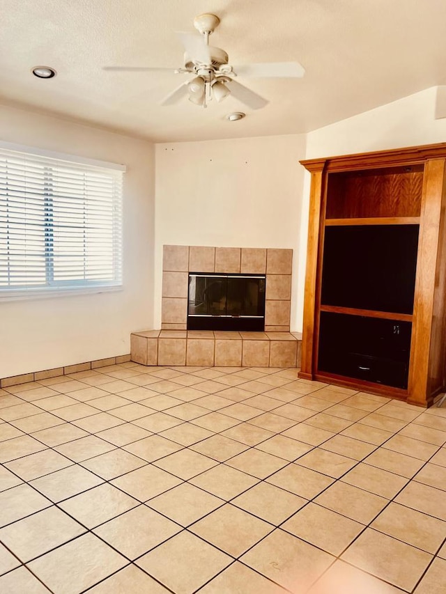 unfurnished living room with ceiling fan, light tile patterned flooring, and a tile fireplace