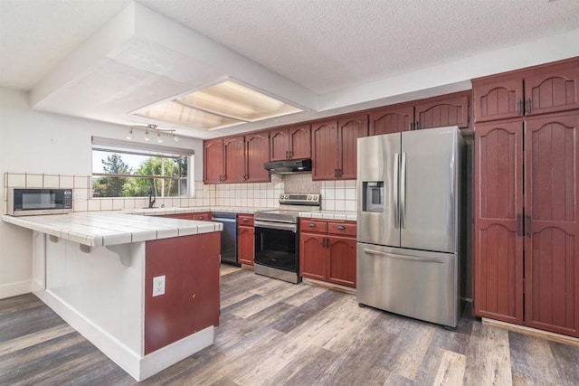 kitchen with stainless steel appliances, tile countertops, decorative backsplash, and kitchen peninsula