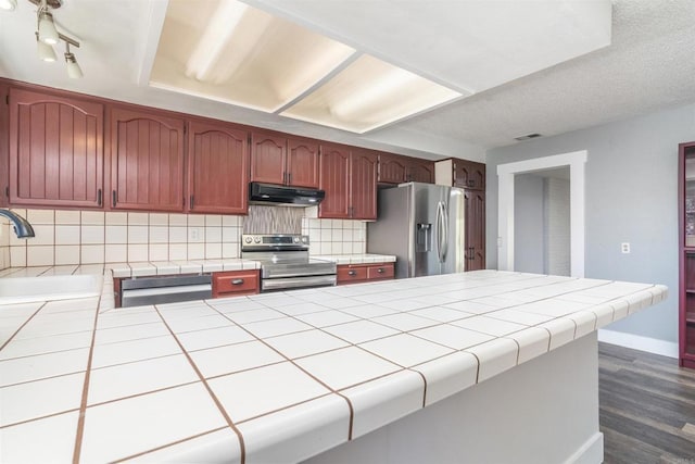 kitchen with appliances with stainless steel finishes, sink, backsplash, dark hardwood / wood-style flooring, and tile counters