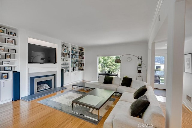 living room featuring hardwood / wood-style flooring, a tiled fireplace, and built in shelves