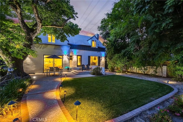 back house at dusk featuring a yard and a patio