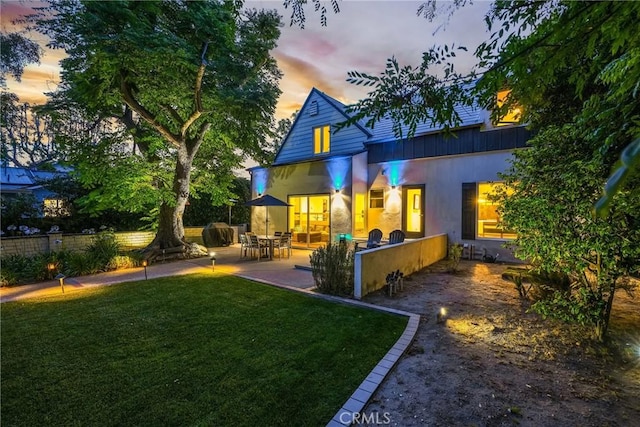 back house at dusk with a patio and a yard